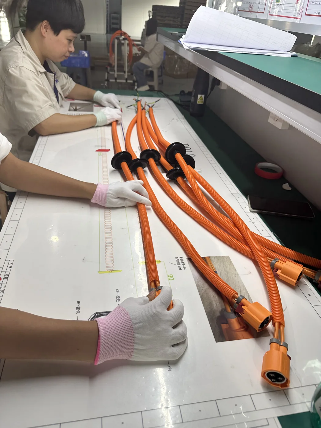 オレンジ色の高電圧ワイヤーハーネスを組み立てる作業者